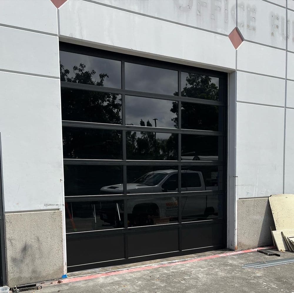 Modern black glass garage door with multiple panels in a commercial building setting.