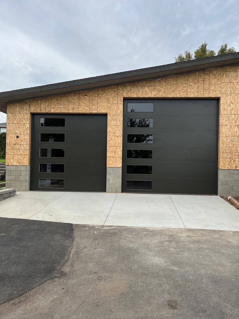 Modern two-car garage with sleek black doors and paneled windows, against a wooden exterior.