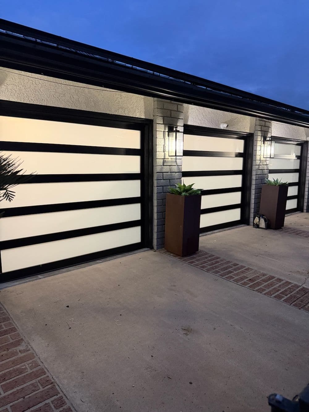 Modern garage doors with horizontal glass panels and stylish planters at dusk.